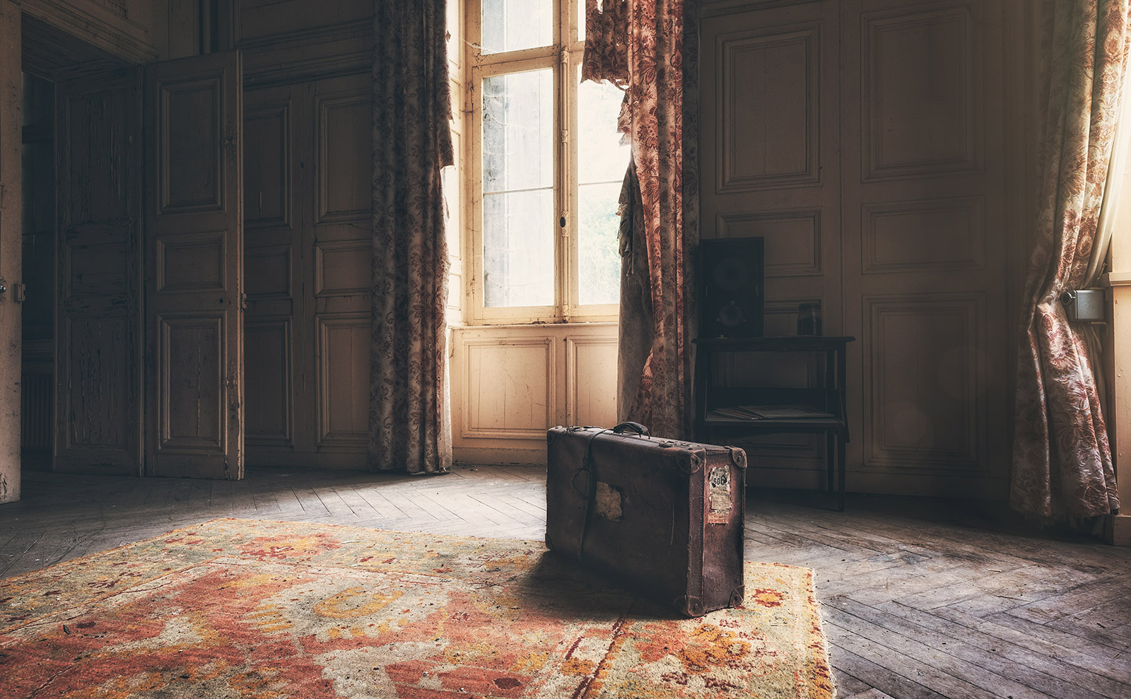 a vintage suitcase sitting on a threadbare oriental rug in an empty room
