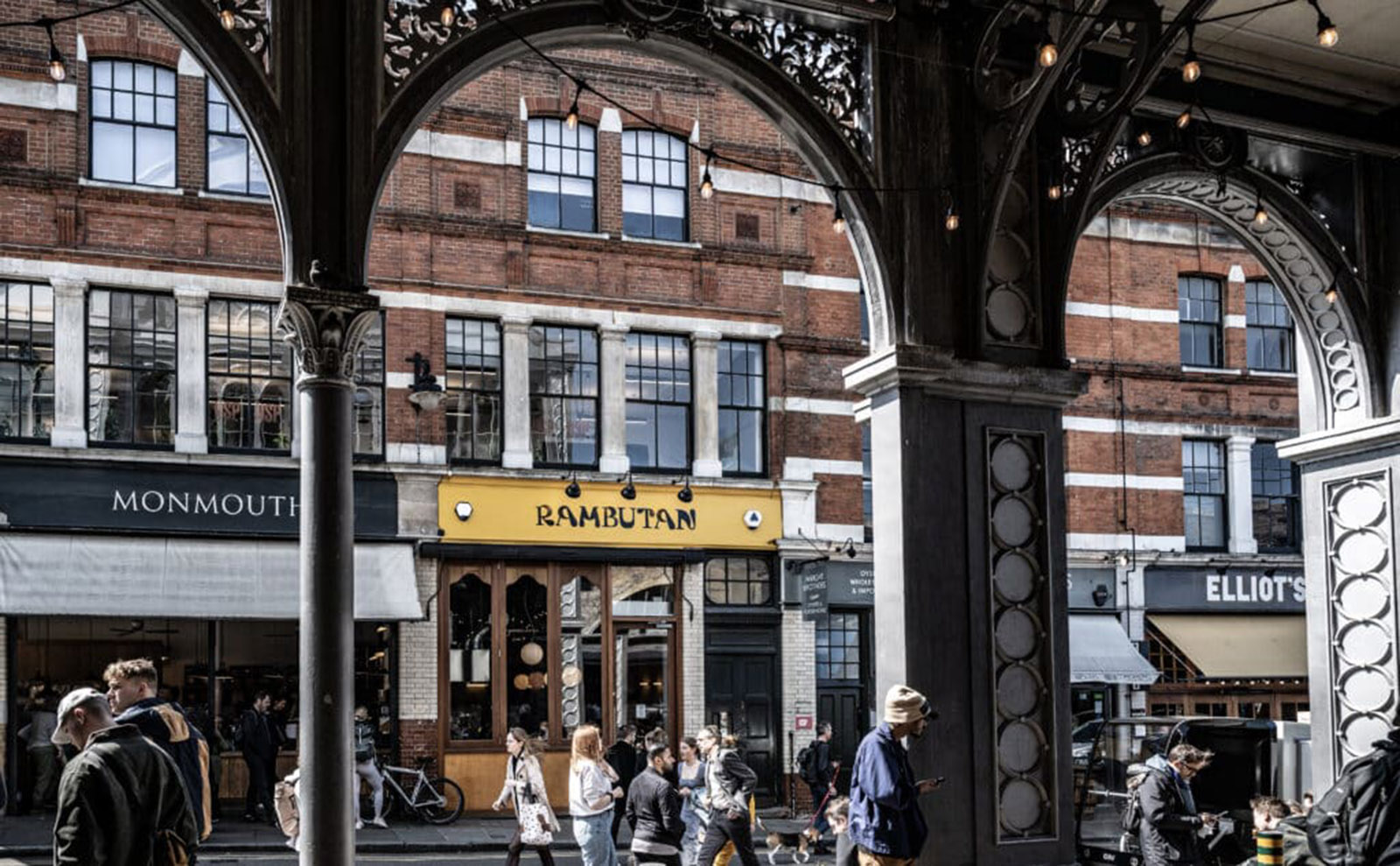 yellow rambutan restaurant sign viewed through the black wrought iron arches of borough market