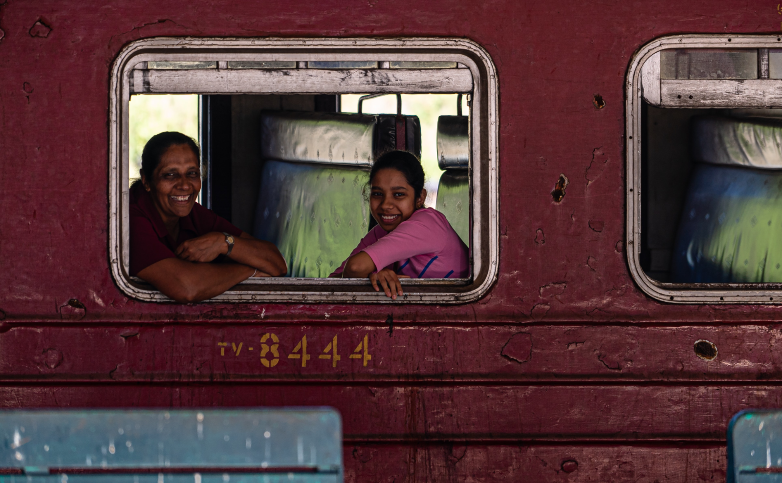 two women sitting in a train and smiling out the window at the camera