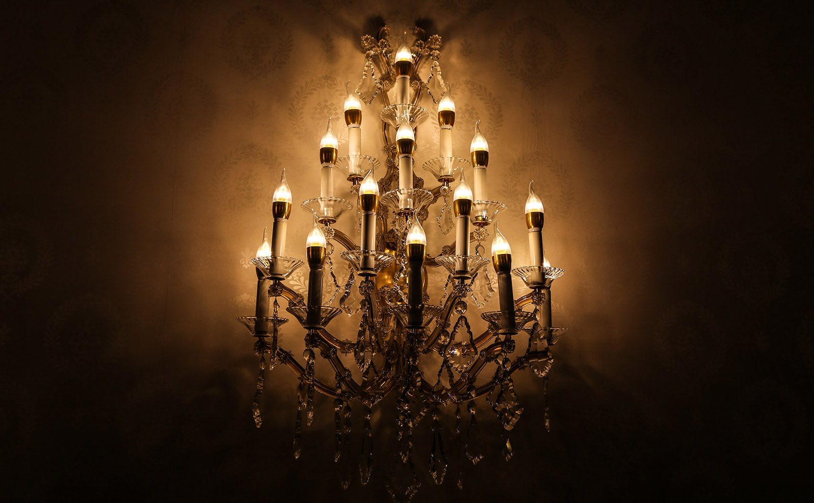 an ornate chandelier with crystals and lit candles hanging against a beige wall